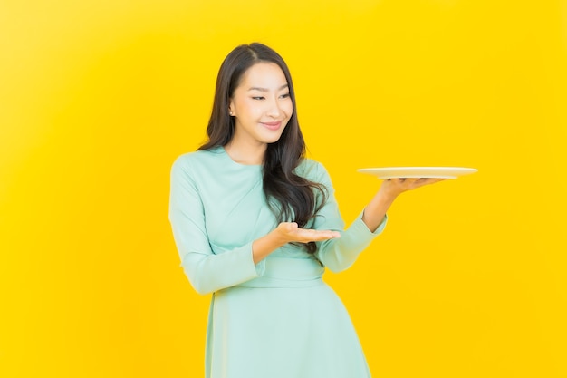 Retrato linda jovem asiática sorrindo com prato vazio em amarelo