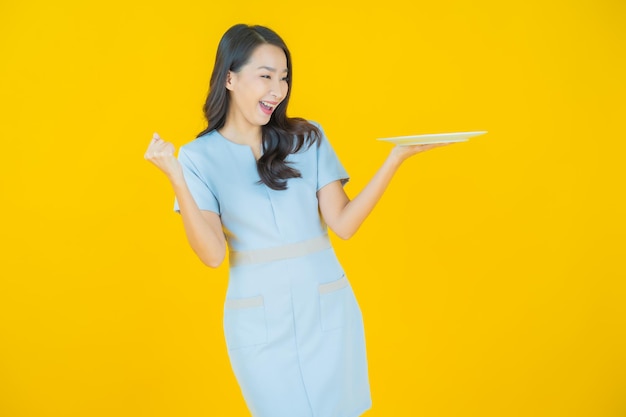Retrato linda jovem asiática sorrindo com prato vazio na cor de fundo.