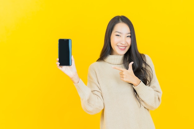 Retrato linda jovem asiática sorrindo com smartphone na parede amarela