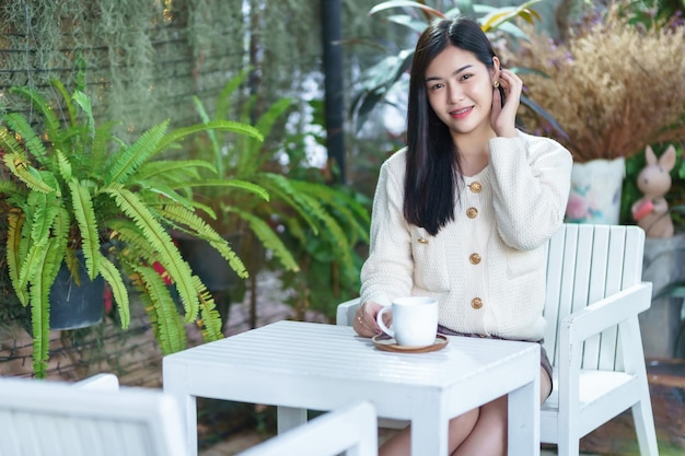 Retrato linda jovem asiática vestindo roupas quentes gosta de beber segurando positivo a xícara de café com leite ou chocolate em casa em casa na sala de estar dentro ou café