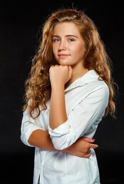 Retrato linda jovem morena com cabelos ondulados em roupas brancas, olhando para a câmera, isolada em fundo escuro