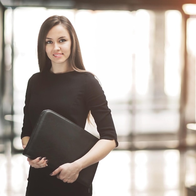 Retrato de una linda joven mujer de negocios sonriendo en la oficina con las manos de la carpeta