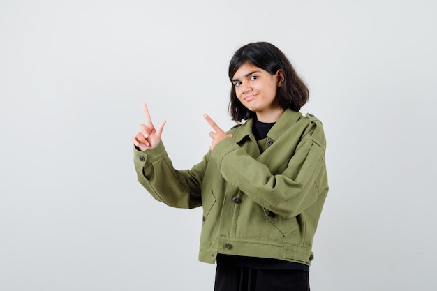 Retrato de linda jovencita apuntando a la esquina superior izquierda en chaqueta verde militar y mirando alegre vista frontal