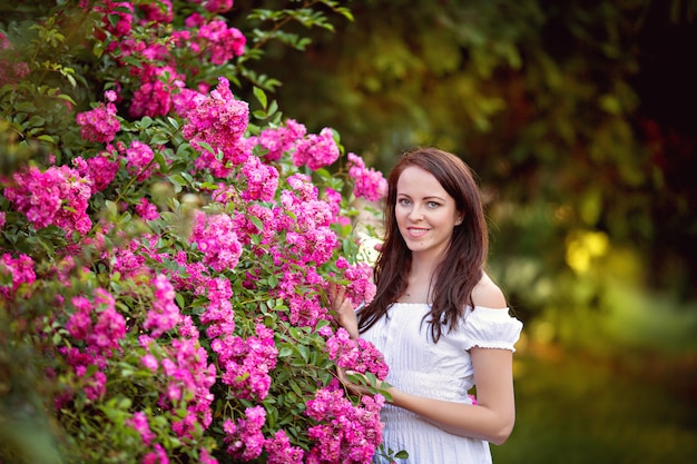 Retrato de una linda morena en un parque de verano cerca de un rosal