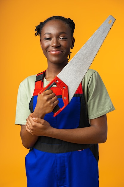 Retrato de una linda mujer afroamericana con uniforme posando con una sierra de madera en sus manos contra