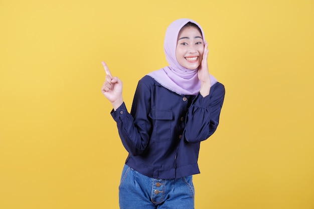 Foto retrato de linda mujer apuntando hacia arriba en tela casual vistiendo hijab sobre fondo amarillo aislado