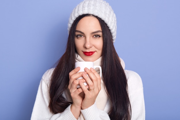 Retrato de linda mujer morena positiva con gorro blanco cálido y suéter