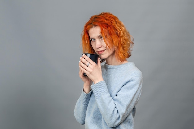 Retrato de una linda mujer pelirroja con ropa informal con una bebida en las manos Mirando la cámara