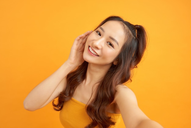 Retrato de una linda mujer sonriente haciendo foto selfie en smartphone aislado sobre un fondo amarillo