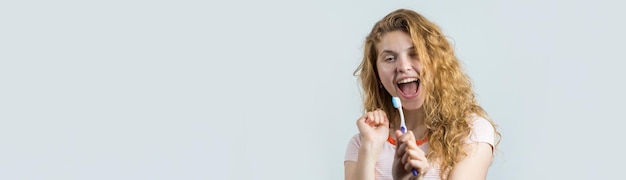 Retrato de una linda mujer sonriente con el pelo rizado rojo sosteniendo un cepillo de dientes aislado en un fondo blanco