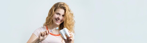 Retrato de una linda mujer sonriente con el pelo rizado rojo sosteniendo un cepillo de dientes aislado en un fondo blanco