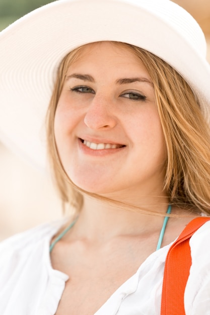 Retrato de linda mujer sonriente con sombrero blanco posando en la playa en día ventoso