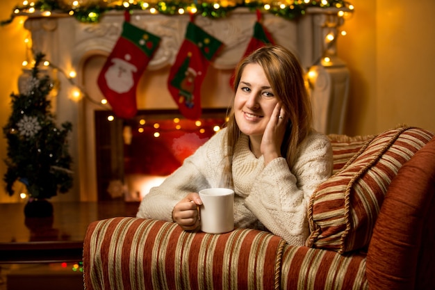 Retrato de linda mujer sonriente sosteniendo una taza de té en la chimenea