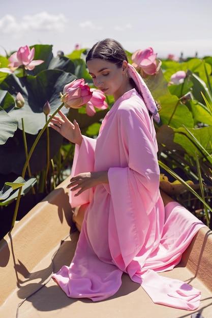 Foto retrato linda mulher morena de vestido rosa está sentada em um barco entre lótus florescendo em um lago em astrakhan