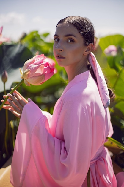 Retrato linda mulher morena de vestido rosa está sentada em um barco entre lótus florescendo em um lago em Astrakhan