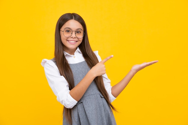 Retrato de una linda niña adolescente que señala con la mano mostrando anuncios con espacio para copiar sobre fondo amarillo Niña feliz que se enfrenta a emociones positivas y sonrientes