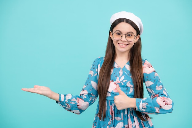 Retrato de una linda niña adolescente señalando con la mano mostrando anuncios con espacio de copia sobre fondo azul Adolescente feliz emociones positivas y sonrientes