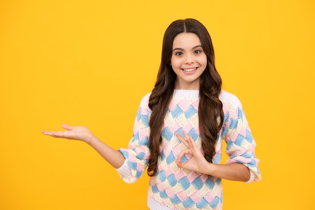 Retrato de una linda niña adolescente señalando con la mano mostrando anuncios con espacio para copiar sobre fondo amarillo