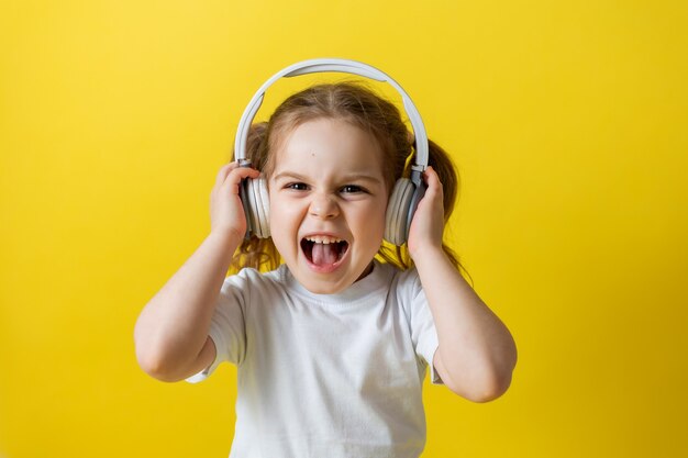 Retrato de una linda niña alegre escuchando música con audiolibros de auriculares blancos