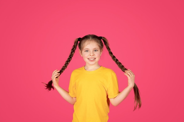 Retrato de linda niña alegre con trenzas posando sobre fondo rosa