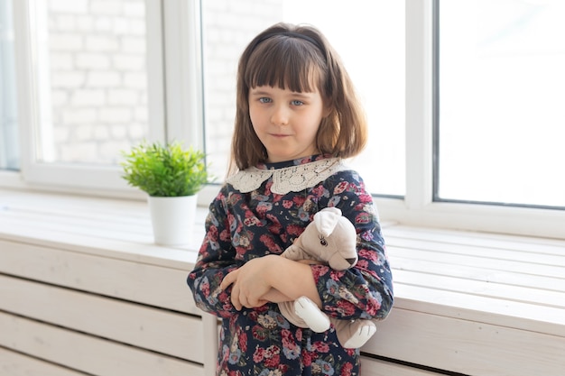 Retrato de una linda niña amable con un vestido de flores con un juguete favorito de conejo suave