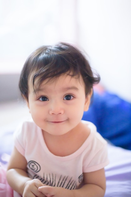 Foto retrato de una linda niña asiática feliz que se sienta en la cama, sonríe y mira a la cámara, concepto de expresión de bebé