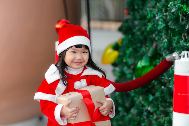 Retrato de una linda niña asiática que usa un vestido de santa feliz cerca del árbol de navidad Niño de Tailandia se une al festival de navidad