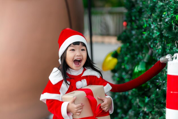 Retrato de una linda niña asiática que usa un vestido de santa feliz cerca del árbol de navidad Niño de Tailandia se une al festival de navidad