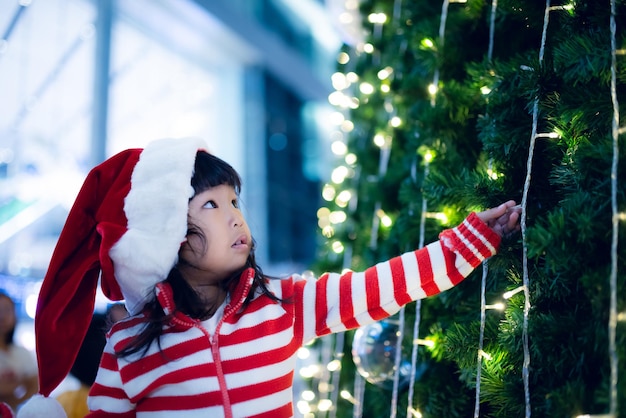 Retrato de una linda niña asiática con sombrero de santa feliz cerca del árbol de navidad Niño de Tailandia se une al festival de navidad