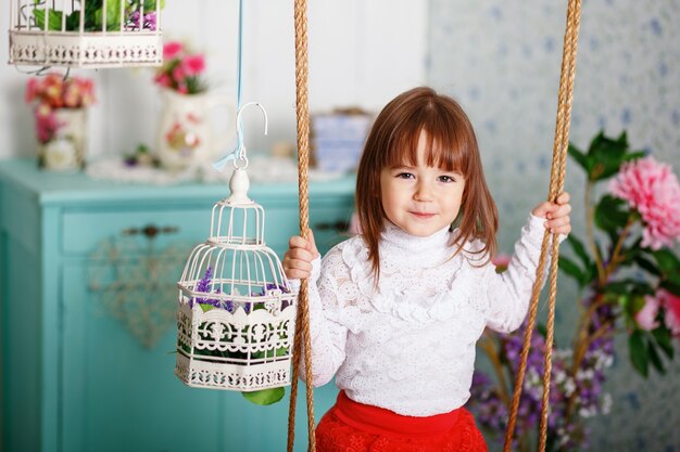 Retrato de una linda niña en un columpio en el interior con una decoración elegante