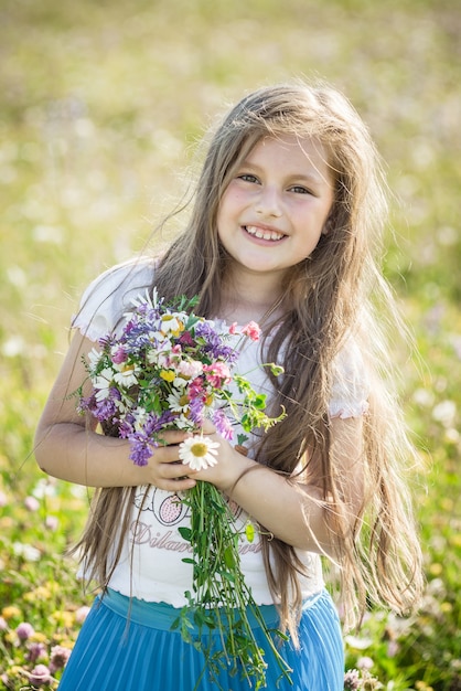 Retrato de una linda niña feliz niño de siete años con flores altramuces en un campo en la naturaleza al aire libre.