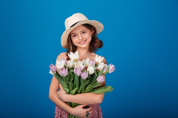 Retrato de linda niña feliz con ramo de flores sobre fondo azul.