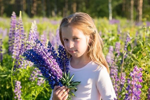 Retrato de una linda niña feliz de siete años con flores de altramuz en el campo de flores de color púrpura Concepto de niño en la naturaleza Vacaciones de verano vacaciones Temporada de alergias de primavera Infancia