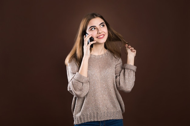 Retrato de una linda niña feliz en suéter hablando por teléfono móvil y riendo aislado sobre fondo de suéter