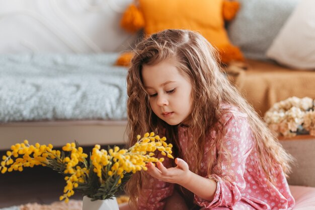 Retrato de una linda niña con flores de mimosa en un dormitorio infantil