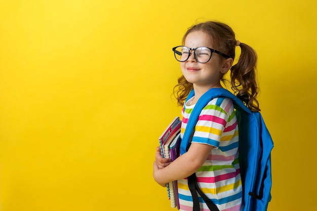 Retrato de una linda niña con gafas en una camiseta a rayas con cuadernos y una mochila