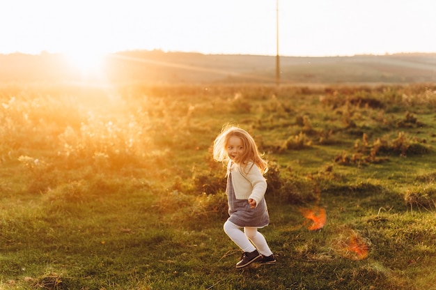 Retrato de una linda niña hermosa y feliz corriendo por el campo soleado