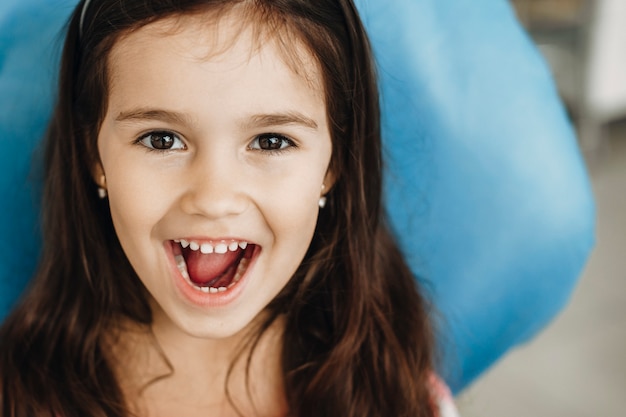 Retrato de una linda niña mostrando los dientes después de la cirugía en una clínica pediátrica de cerca. Niño feliz después del examen de los dientes.