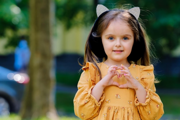 Retrato de una linda niña en el parque y muestra un signo de corazón con las manos