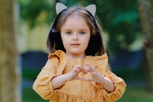 Retrato de una linda niña en el parque y muestra un signo de corazón con las manos