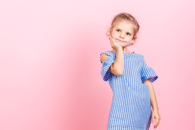 Retrato de una linda niña pequeña que viste un vestido azul mientras posa sobre un fondo rosa de estudio