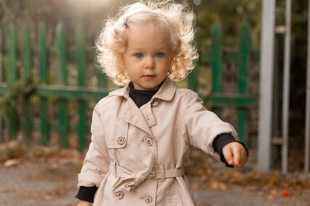 Retrato de una linda niña rubia rizada con ojos azules en un impermeable de lino blanco