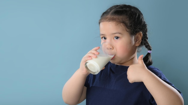 Retrato de una linda niña satisfecha con un vaso de leche aislado sobre fondo azul.