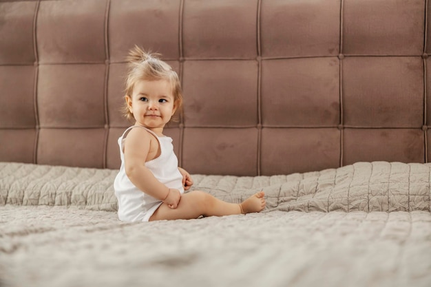 Retrato de una linda niña sentada en la cama en el dormitorio y mirando por encima del hombro