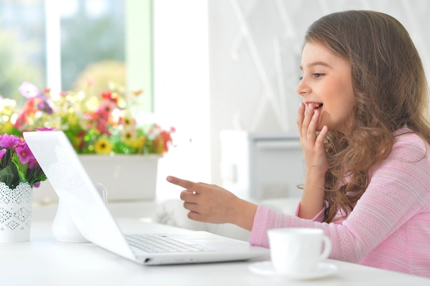 Retrato de una linda niña sentada en la mesa con una laptop