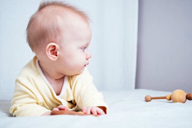 Retrato de una linda niña de siete meses con ojos azules. Un niño juega con juguetes de madera en una habitación luminosa. Juguetes ecológicos para niños fabricados con materiales naturales.