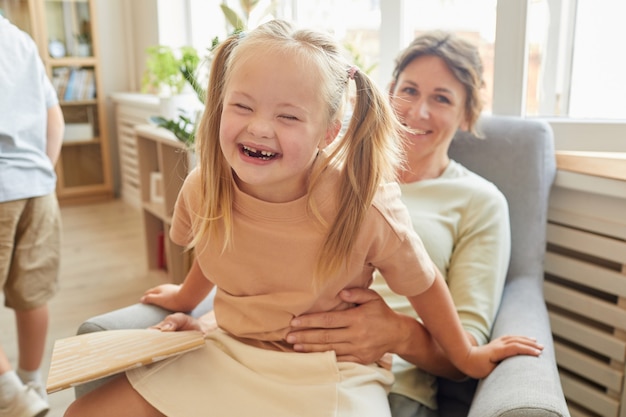 Retrato de linda niña con síndrome de down riendo alegremente mientras juega con la madre en casa