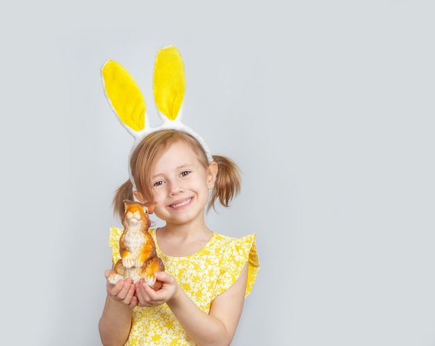 Retrato de una linda niña sonriente caucásica con orejas de conejo y adornos para la Pascua en las manos.