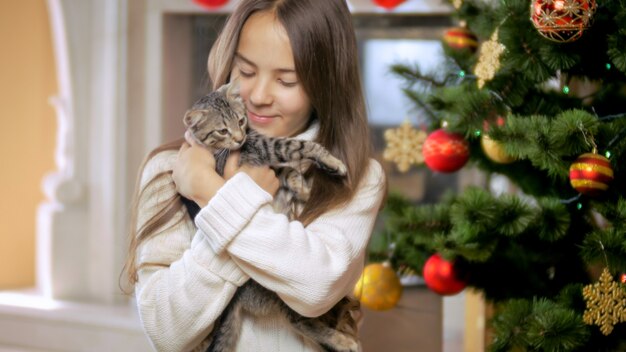 Retrato de linda niña sonriente celebrando la Navidad con lindo gatito gris