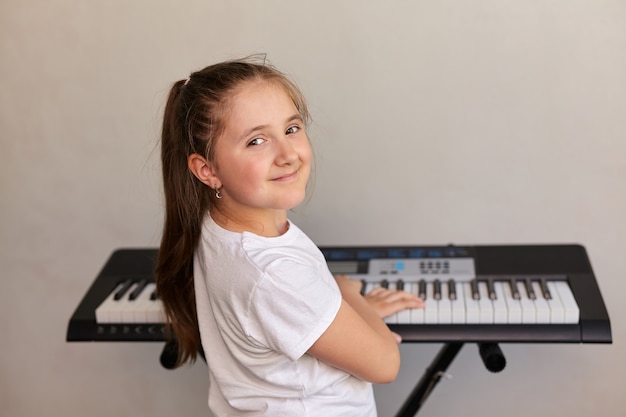 Retrato de linda niña sonriente feliz tocando el piano eléctrico